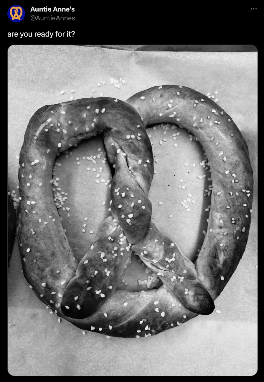 A screenshot of a post on X (formerly Twitter) from Auntie Anne's. The caption reads, "are you ready for it?" and is accompanied by a black and white photo of a delicious-looking soft pretzel.